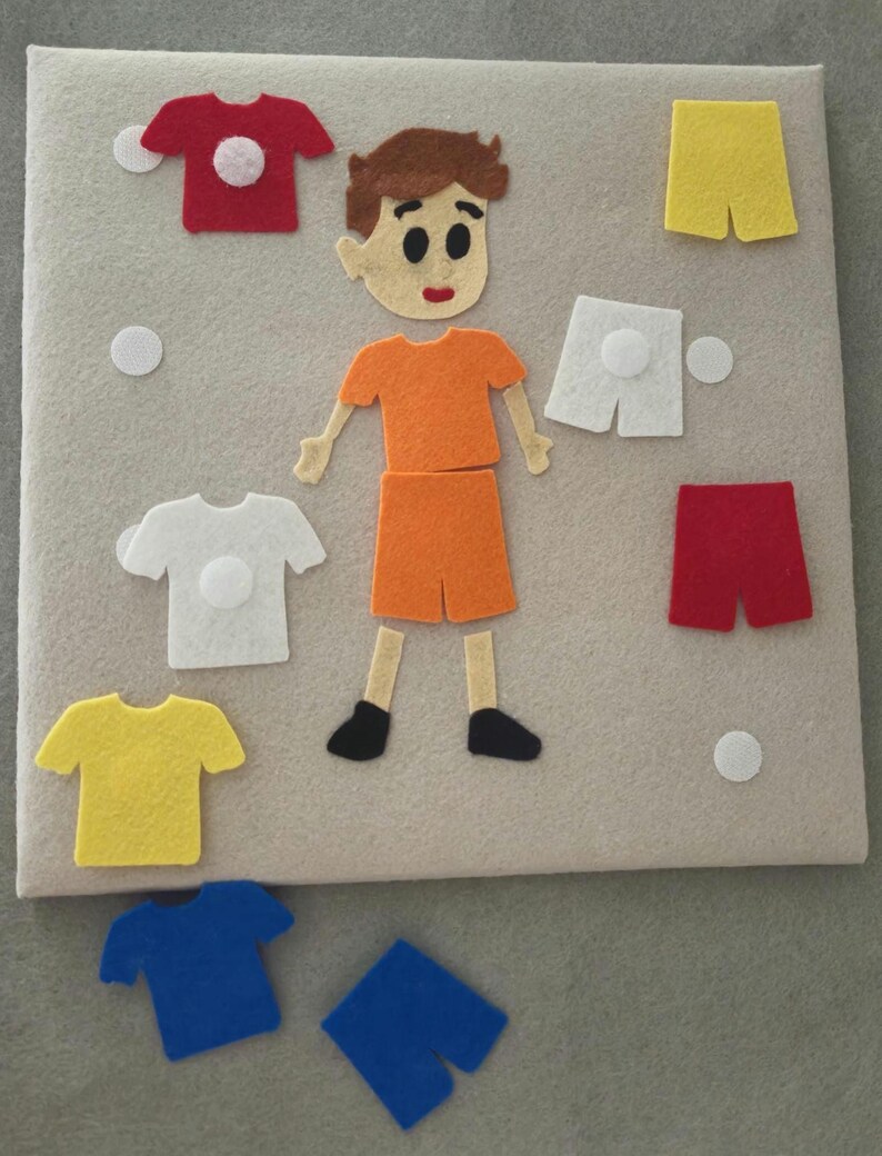 May include: A felt board with a cartoon figure and various felt clothing items. The figure is wearing an orange shirt and shorts. There are red, white, yellow, and blue shirts and shorts. White felt circles are also included.