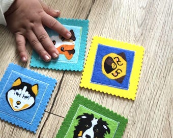 May include: Four colorful felt squares with dog faces. The squares are blue, yellow, and green, with a light blue square being touched by a hand. The dog faces include a husky, a border collie, and a fox-like dog.