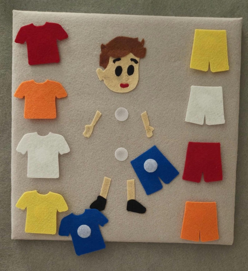 May include: A felt board with a boy's face, arms, legs, and various colored shirts and shorts. The shirts are red, orange, white, yellow, and blue. The shorts are yellow, white, red, and orange. The board is beige.