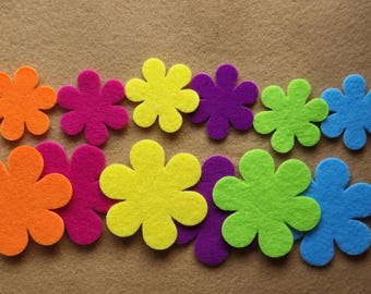 May include: A collection of colorful felt flower cutouts in orange, fuchsia, yellow, purple, green, and blue. The flowers are arranged on a tan background. These craft supplies are ideal for various DIY projects.