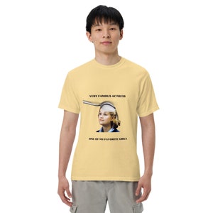 May include: A pale yellow t-shirt with a graphic of a woman in a hat and the text "VERY FAMOUS ACTRESS" and "ONE OF MY FAVORITE GIRLS". The shirt is worn by a person.