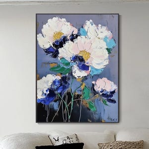 Puede incluir: Una pintura floral abstracta con grandes flores texturizadas blancas, rosas y azules con centros amarillos sobre un fondo azul apagado. La obra de arte se exhibe en un salón, encima de un sofá blanco.