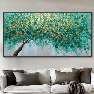 Könnte beinhalten: Große rechteckige Leinwandkunst mit einem Baum mit braunem Stamm und türkis-goldenen Blättern. Das Gemälde ist vor einem hellgrauen Hintergrund platziert und schwarz gerahmt. Das Kunstwerk hängt über einem weißen Sofa.