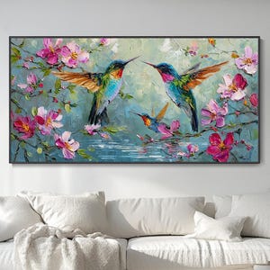 Puede incluir: Un cuadro rectangular de pared con una pintura al óleo de tres colibríes en vuelo entre flores rosas y blancas. Las aves muestran un plumaje vibrante en verde, azul y naranja, sobre un fondo suave y texturizado de tonos apagados.