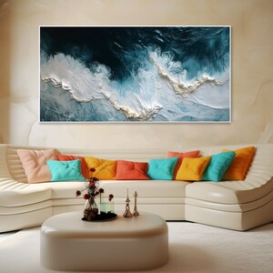 May include: Abstract painting of blue and white waves, framed and hanging on a wall above a white couch with colorful pillows.
