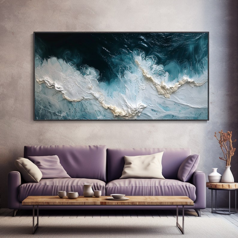 May include: Abstract painting of ocean waves in shades of blue, white, and gold. The painting is framed in black and hangs on a wall above a purple sofa.