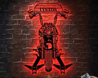 May include: A black metal motorcycle silhouette with the name "LYTON" on the front, illuminated in red. The motorcycle has a headlight and handlebars. The image includes a remote control with colored buttons.