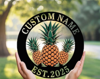 May include: A round, black metal sign featuring three pineapples with green leaves and orange bodies. The words "CUSTOM NAME" and "EST. 2025" are in a circular design around the pineapples. The sign is held up by two hands.