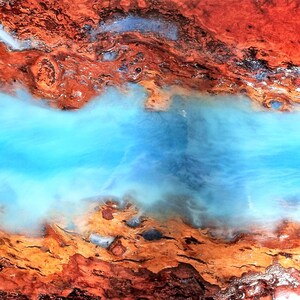 May include: Abstract art painting with a blue resin pour over a brown and orange wood background.