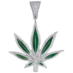 Puede incluir: Colgante de plata con forma de hoja de cannabis, con esmalte verde e incrustaciones de pequeñas piedras preciosas transparentes. El colgante tiene una argolla en la parte superior para una cadena.