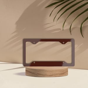 May include: A brown metal license plate frame with rounded corners and four screw holes. The frame is sitting on a wooden platform.