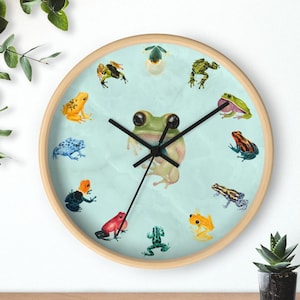 May include: A light blue clock face with a green frog in the center. The clock is surrounded by 12 frogs in various colors and poses. The clock is made of wood and has a white background.