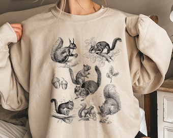 May include: A beige sweatshirt with a vintage illustration of squirrels and acorns. The squirrels are in various poses, including climbing trees and holding acorns.
