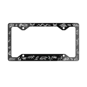 May include: Black metal license plate frame with a white outline and various animal illustrations, including a snake, a butterfly, a turtle, a deer, and a bird.
