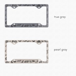 May include: Two license plate frames with a gray and pearl gray finish. Both frames feature a decorative border of various animals, including a snake, a butterfly, a squirrel, a deer, and a turtle.