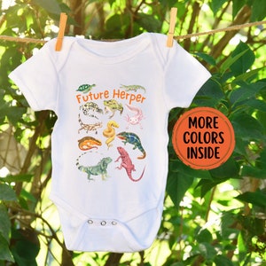 May include: White baby onesie with the text "Future Herper" in orange. The onesie features a colorful illustration of various reptiles and amphibians, including a turtle, frog, salamander, lizard, and snake.