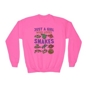 May include: Pink sweatshirt with the text "Just a girl who loves snakes" and a graphic of various snakes in different colors.