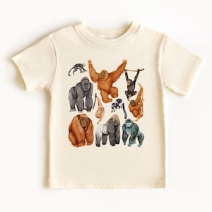 May include: A cream-colored t-shirt with a colorful illustration of various primates, including gorillas, orangutans, and monkeys. The illustration is in a watercolor style and features a variety of poses and expressions.