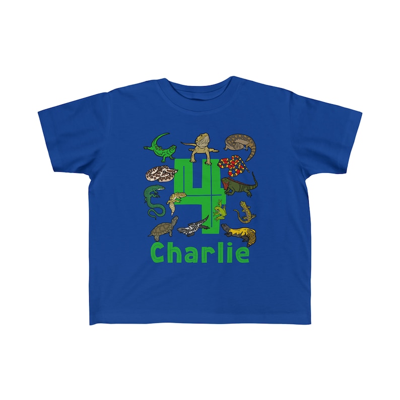 K&ouml;nnte beinhalten: Ein k&ouml;nigsblaues T-Shirt mit einer gr&uuml;nen Zahl vier, die von Comic-Reptilien umgeben ist. Der Text "Charlie" ist unter der Zahl gedruckt.
