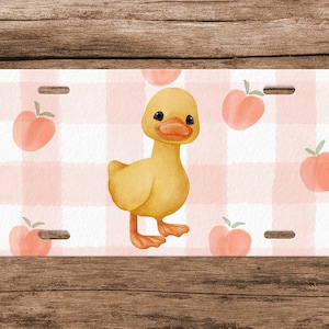 May include: A yellow duckling with a pink and white gingham background. The background is decorated with peach illustrations.