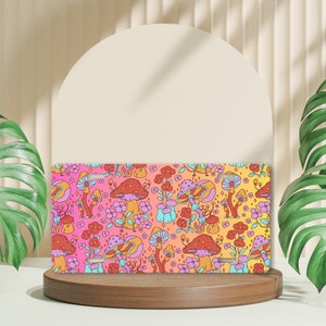 May include: A license plate featuring a vibrant, psychedelic mushroom pattern in shades of pink, orange, and yellow. The design includes various mushroom illustrations, flowers, and sparkling accents, creating a whimsical and colorful aesthetic.