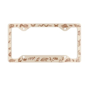 May include: A cream-colored metal license plate frame with a brown outline. The frame is decorated with a variety of animals, including a snake, a butterfly, a squirrel, a turtle, a deer, a duck, and a rabbit.