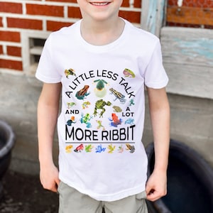 K&ouml;nnte beinhalten: Wei&szlig;es T-Shirt mit einem Kreisdesign mit Fr&ouml;schen und dem Text "A little less talk and a lot more ribbit".