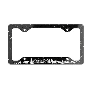 May include: Black license plate frame with a starry night sky design. The bottom of the frame features a silhouette of a forest, mountains, and wolves howling at the moon. The frame has four mounting holes.
