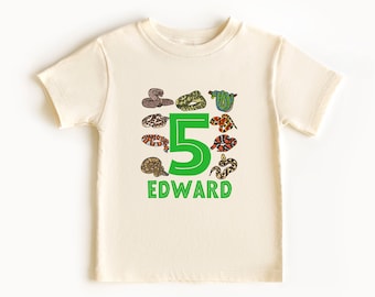 Könnte beinhalten: Ein hellbeiges T-Shirt mit einer grünen Zahl 5 und dem Namen "EDWARD" darauf gedruckt. Die Zahl 5 ist von bunten Comic-Schlangen umgeben.