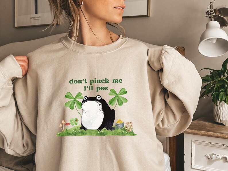 May include: A beige sweatshirt with a graphic of a black frog with the text "don't pinch me I'll pee" and green shamrocks.