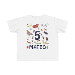 May include: White t-shirt featuring a colorful insect and bug design. The number "5" is prominently displayed, along with the name "MATEO" in navy blue. Various insects, including butterflies, beetles, and dragonflies, are scattered around the number.