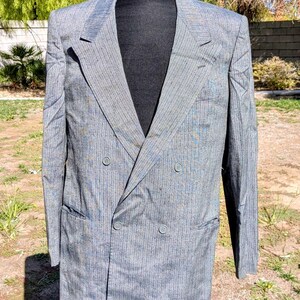 Peut inclure: Un blazer gris à double boutonnage avec un motif à rayures subtiles. La veste présente un revers cranté, deux rangées de boutons et deux poches avant. Le blazer est présenté sur un mannequin noir.