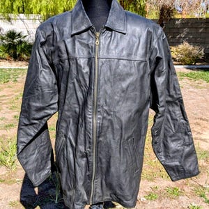 May include: A black leather jacket with a collared neckline and a full-length zipper. The jacket has two front pockets and is displayed on a black mannequin. The jacket appears to be made of a soft, supple leather.