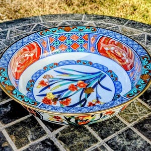 May include: A decorative ceramic bowl with a detailed floral and bird design. The bowl features a gold rim and a vibrant color palette of blue, red, and orange. The interior showcases a floral motif with a white background.
