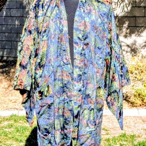May include: A long, open-front robe with a vibrant floral pattern in shades of blue, green, red, and yellow. The robe is displayed on a black mannequin, showcasing its flowing design and intricate details. The fabric appears to be silky.