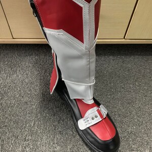 K&ouml;nnte beinhalten: Rote und wei&szlig;e Stiefel mit schwarzer Sohle und einer Schnalle oben. Die Stiefel haben einen wei&szlig;en Besatz am oberen Rand und ein rotes und wei&szlig;es Muster an der Seite.