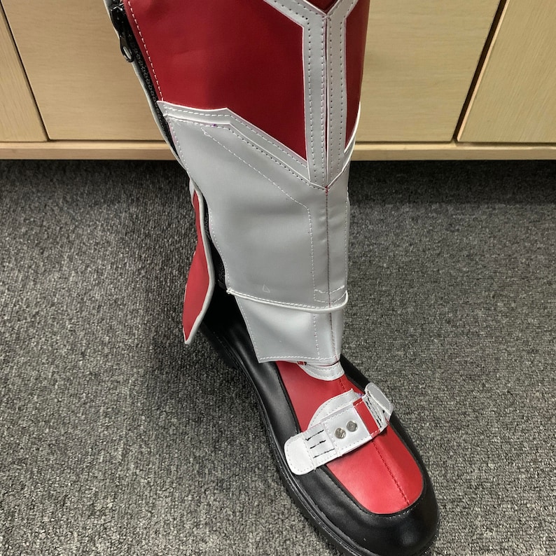 K&ouml;nnte beinhalten: Rote und wei&szlig;e Stiefel mit schwarzer Sohle und einer Schnalle oben. Die Stiefel haben einen wei&szlig;en Besatz am oberen Rand und ein rotes und wei&szlig;es Muster an der Seite.