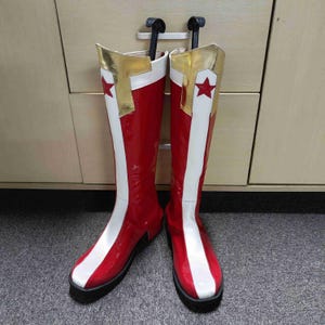 Puede incluir: Un par de botas rojas y blancas de caña alta con una estrella dorada en cada bota.