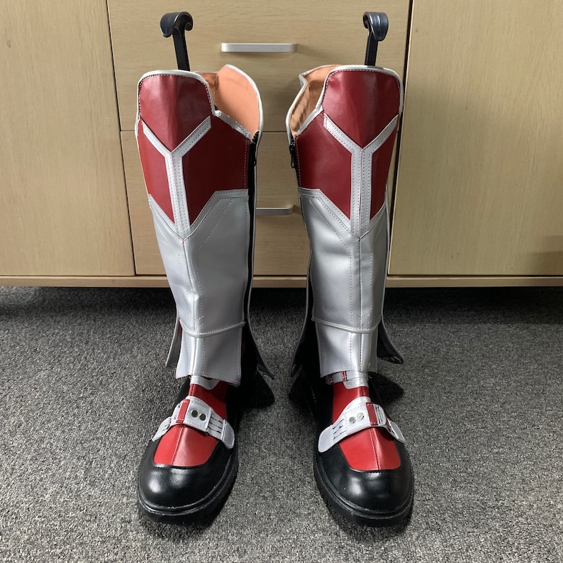 K&ouml;nnte beinhalten: Ein Paar rot-silberne Stiefel mit schwarzen Sohlen. Die Stiefel haben eine spitze Zehenpartie und einen Rei&szlig;verschluss an der Innenseite des Kn&ouml;chels.