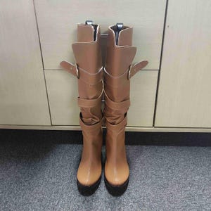 Peut inclure: Une paire de bottes en cuir marron montant au genou avec des boucles et un petit talon.