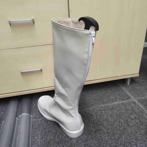 Op de afbeelding: Een lichtgrijze hoge laars met een witte zool en een rits aan de zijkant. Er zit een zwarte schoenspanner in om de vorm van de laars te behouden. De laars is gemaakt van een glad, synthetisch materiaal.