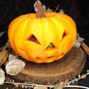 Könnte beinhalten: Ein geschnitzter, orangefarbener Kürbis mit dreieckigen Augen und einem lächelnden Mund, ideal für Halloween. Der Kürbis steht auf einer Holzscheibe, mit einem braunen Stiel und einem farbenfrohen Inneren.