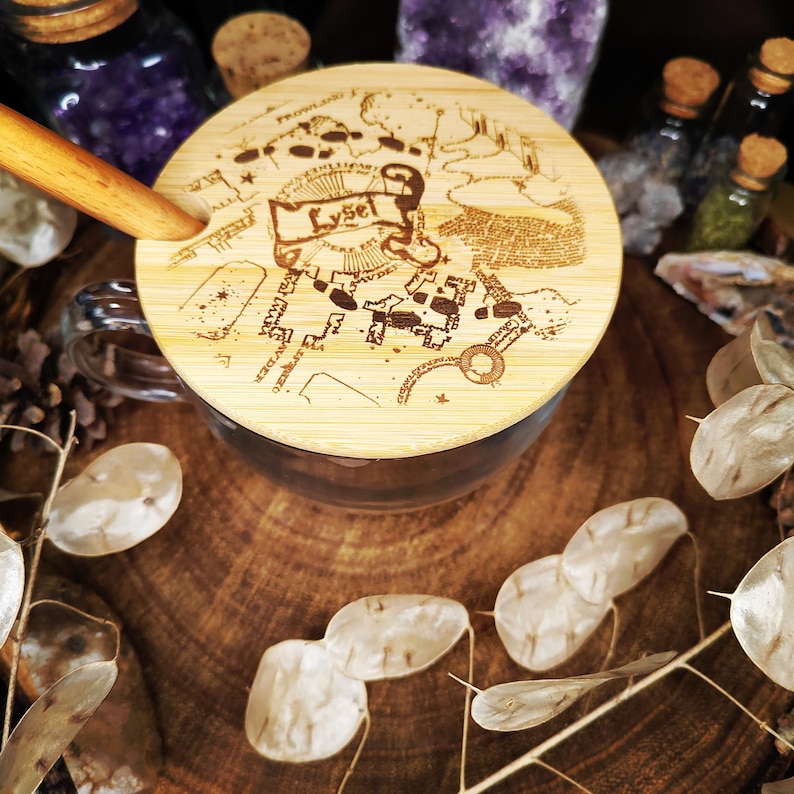 Puede incluir: Una tapa de madera con un dise&ntilde;o de mapa y la palabra "Lysel" grabada en ella. La tapa est&aacute; sobre una taza de vidrio transparente con un asa de madera.