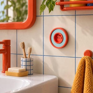 Può includere: Una parete del bagno con piastrelle quadrate bianche e fughe blu, uno specchio con cornice arancione, un rubinetto arancione, un portasapone giallo con una saponetta, un portaspazzolini a griglia blu e bianca e una presa elettrica arancione e azzurra.