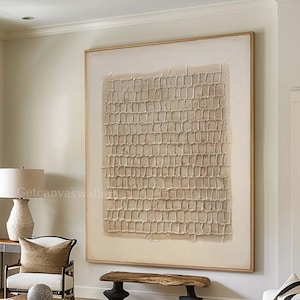 May include: A large rectangular wall art piece featuring a textured, grid-like pattern in beige and cream tones, framed in light wood. The artwork displays a raised, tactile surface with repeating square shapes centred on a plain background.