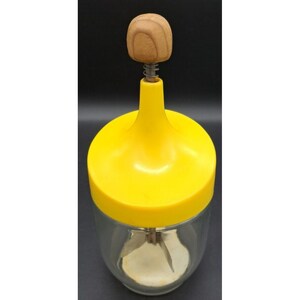 May include: A vintage yellow and clear glass food chopper with a wooden knob handle. The chopper has a yellow lid and a spring mechanism. The glass jar is clear, and the blades are visible inside.