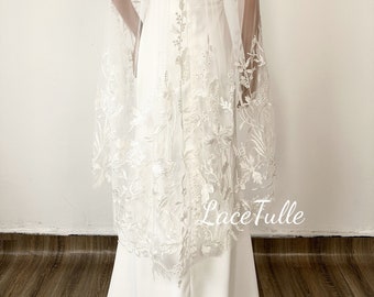 May include: A white bridal veil with delicate floral lace trim. The veil is made of soft tulle and has a scalloped edge. The veil is shown from the back, with the lace trim visible along the bottom edge.