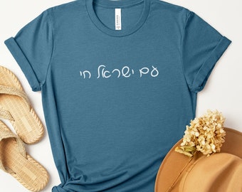 May include: A teal blue t-shirt with the Hebrew phrase "In silence, I" printed in white on the front.