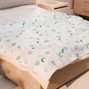 May include: A white bedspread featuring a repeating pattern of green icons, such as stars, moons, and geometric shapes, covers a bed. The bed is made up with a white sheet and sits on a beige bed frame. The room has a neutral colour palette.