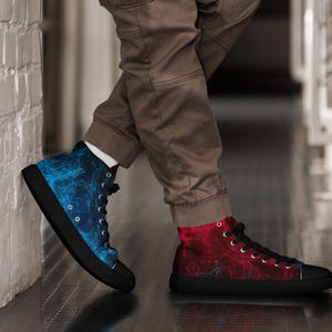Puede incluir: Zapatillas altas con suela y cordones negros. Un zapato es azul con un diseño de red, el otro es rojo con un patrón similar. Los zapatos los lleva una persona con pantalones marrones.
